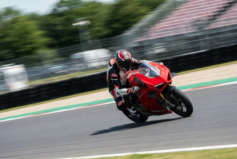 Track rider leaning on sportbike at speed wearing full-face helmet on racetrack