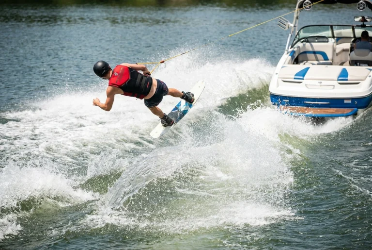 Wakeboarder jumping wake behind boat wearing water-sports helmet and life vest